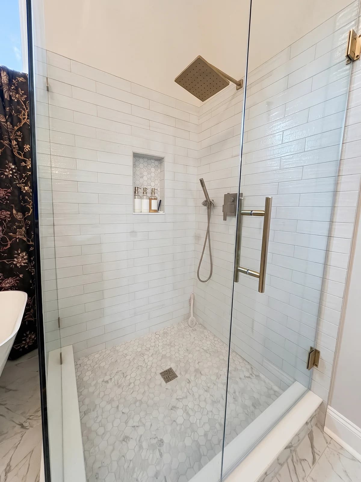 Walk-in shower with white subway tile walls, a recessed niche, a hexagon mosaic floor, and a frameless glass door
